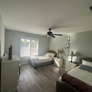 A modern bedroom featuring two twin beds, a ceiling fan, and ample natural light filtering through the windows.