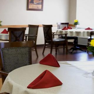 A cozy dining area with neatly set tables featuring red napkins and floral centerpieces.