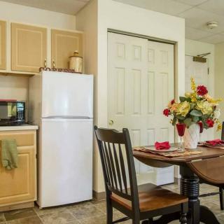 A cozy kitchen and dining area featuring a table with flowers, chairs, a refrigerator, cabinets, and a microwave.