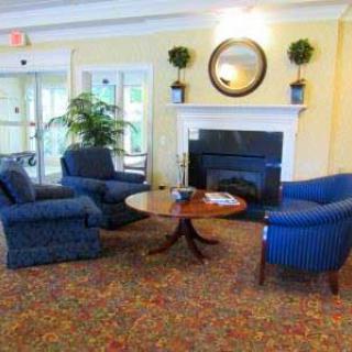 A cozy living room with a seating area featuring blue armchairs and a coffee table, centered around a fireplace with a mirror above it.