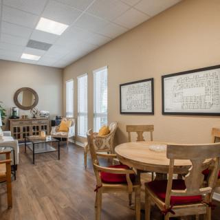 A cozy dining room with wooden floors, featuring a round table and chairs, adorned with wall art and a mirror.