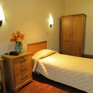 A cozy bedroom featuring a single bed, wooden furniture, and decorative flowers.