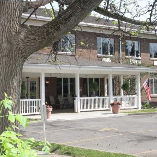 A two-story residential building with a front porch and a tree in the foreground.