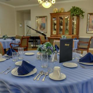 An elegantly set dining room with blue-themed table settings and a piano in the background.
