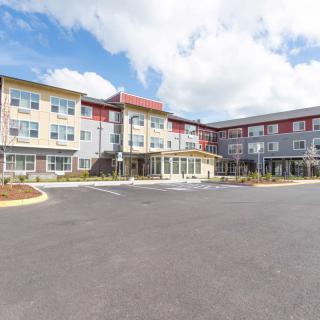 A modern hotel building with a spacious parking lot under a partly cloudy sky.