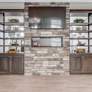 A modern living room with a stone fireplace, built-in shelves, and a large television.