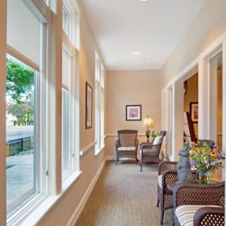 A bright hallway with large windows, featuring comfortable seating and artwork.