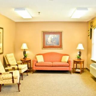 A cozy living room with a pink sofa, two armchairs, side tables with lamps, and a framed painting on the wall.