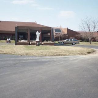 A building with a statue in front, a parked car, and an open roadway.
