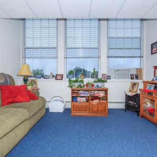 A cozy office space with a couch, bookshelves, and large windows.