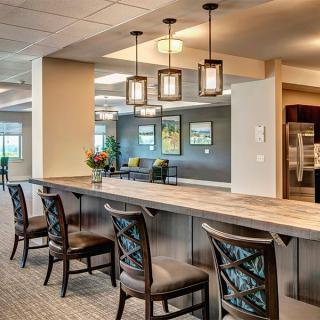 A modern kitchen interior with a long counter and stylish bar stools, illuminated by pendant lights.