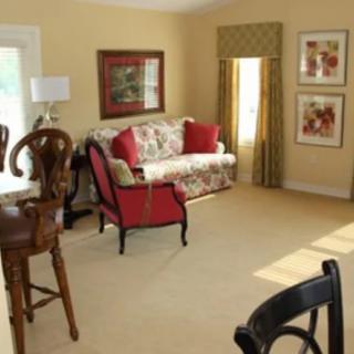 A cozy living room with a floral sofa, red armchair, and framed artwork on the walls.