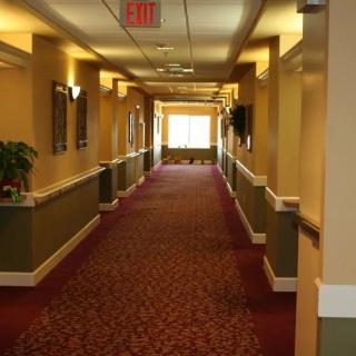 A well-lit hallway with a patterned carpet and wall sconces.
