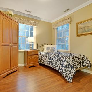 A cozy bedroom with a single bed, wooden furniture, and large windows bringing in natural light.