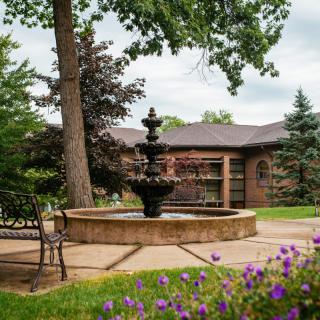 A tranquil garden scene with a central fountain, surrounded by trees and blooming flowers.