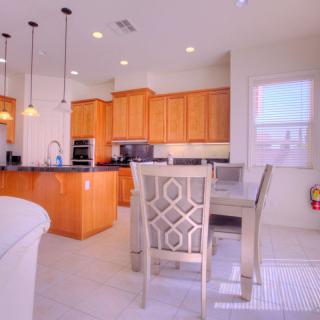 A modern kitchen with wooden cabinets and a dining area, featuring pendant lighting and bar stools.