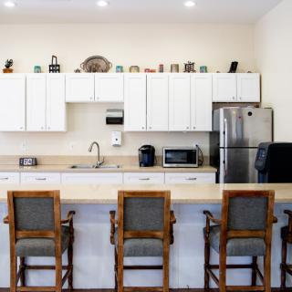 A modern kitchen with a clean countertop and high chairs, featuring sleek white cabinets and stainless steel appliances.