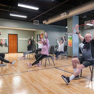 A group of senior citizens engaged in a chair-based exercise class indoors, focusing on health and fitness.