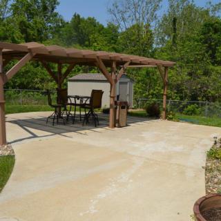 A backyard patio with a pergola and outdoor seating area amidst greenery.
