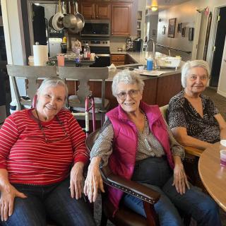 Three elderly women sitting together in a cozy kitchen setting.