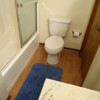 A bathroom featuring a toilet, bathtub, and a blue rug on wooden flooring.