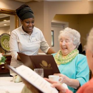 A caregiver assisting an elderly woman with a menu at a senior living facility.