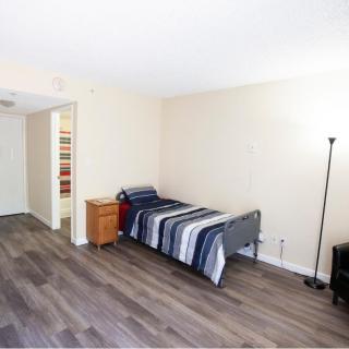 A minimalist bedroom featuring a single bed and a floor lamp on wooden flooring.