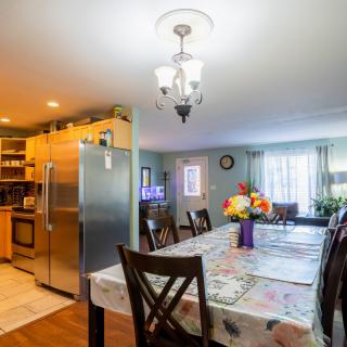 A cozy dining area with a table and chairs next to a modern kitchen, featuring a chandelier and floral centerpiece.