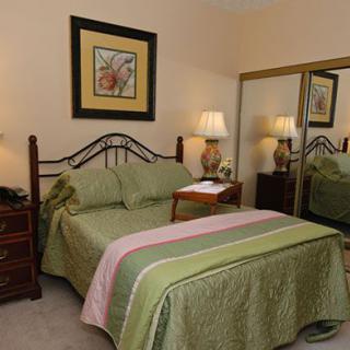 A cozy bedroom with a neatly made bed, mirrored closet, and decorative lamps.