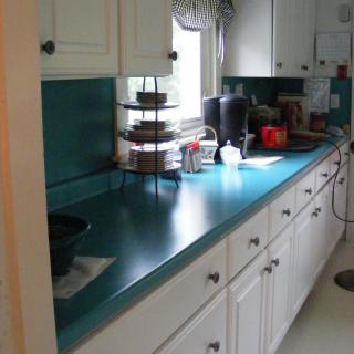 A kitchen with teal countertops and white cabinets, featuring various appliances.
