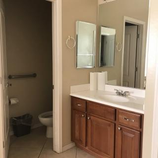 A clean and well-organized bathroom featuring a sink with a wooden cabinet, a mirror, and a toilet in an adjacent space.