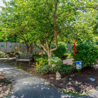 A peaceful garden with a pathway winding through lush greenery and trees, featuring a bench for relaxation.