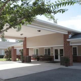 The image shows the entrance of a building with a covered driveway, surrounded by trees.