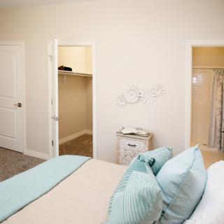 A serene and minimalist bedroom featuring a neatly made bed with pastel-colored pillows and two closet doors.