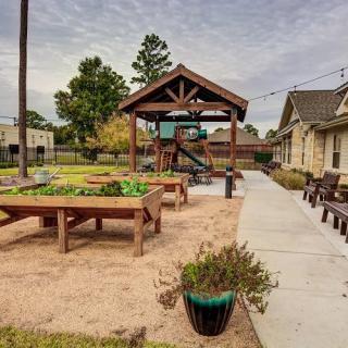 A community outdoor area featuring a playground, benches, and garden plots.