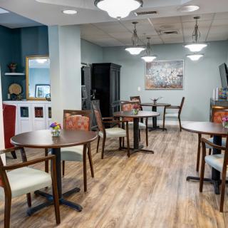 A modern dining area with neatly arranged tables and chairs, featuring elegant lighting and a wooden floor.