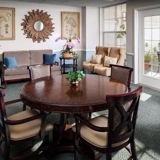 A cozy living room featuring a round wooden table surrounded by chairs, with a couch and armchairs near the window.