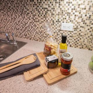 A kitchen countertop with cooking essentials including wooden utensils, pasta, olive oil, and canned food against a mosaic-tiled backsplash.