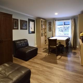 A cozy living room with wooden flooring, a dining table near the window, and art adorning the walls.