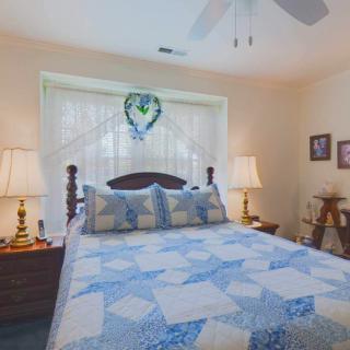 A cozy bedroom with a blue-patterned quilt, two nightstands with lamps, and a decorative window.