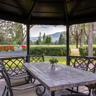 A peaceful gazebo with a stone table and chairs, offering a scenic view of the garden and distant mountains.