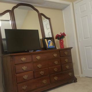A bedroom dresser with a mirror, television, and a vase of flowers.