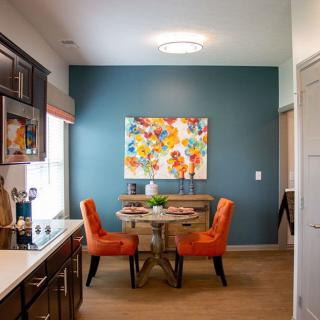A modern kitchen dining area featuring vibrant orange chairs and colorful artwork on a blue accent wall.