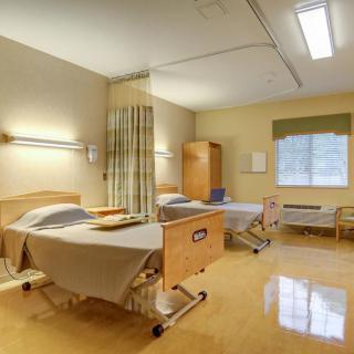 An empty hospital room with two beds, bright lighting, and a window.