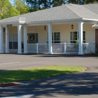 A residential building with a porch and columns, surrounded by greenery.