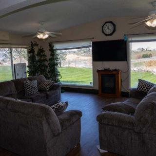 A cozy living room with large windows, featuring comfortable sofas, a television, and a fireplace.