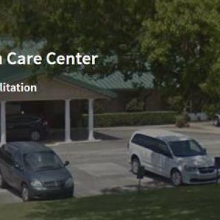 A healthcare center with parked vehicles in front and surrounded by trees.