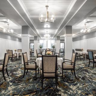 Elegant dining area with neatly arranged tables and chairs, featuring sophisticated lighting and patterned carpet.
