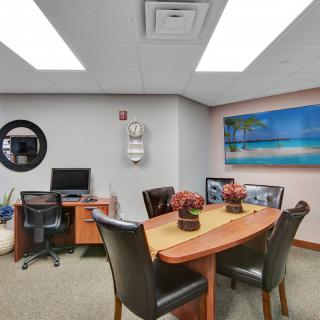 A small office meeting room with a conference table, chairs, and a computer desk.