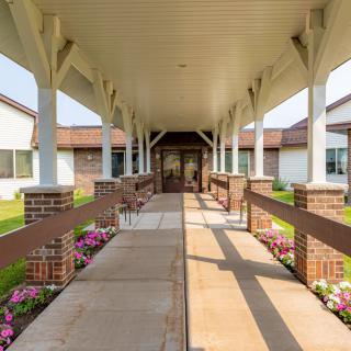 A covered walkway leads to the entrance of a building, flanked by flower beds.